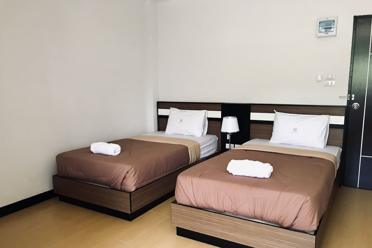 A hotel room with two beds, each with a brown bedspread and white pillows, and a small bedside table with a lamp.