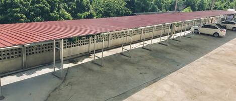 Un estacionamiento con techo rojo y suelo de concreto, rodeado de vegetación y edificios.