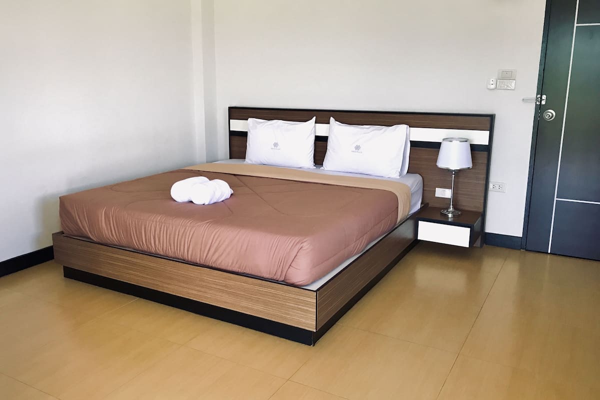 A neatly made bed with a brown cover and white pillows, a bedside table with a lamp, and a door to the right.
