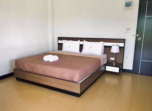 Un lit bien fait, recouvert d’une couverture marron et agrémenté d’oreillers blancs, une table de chevet avec une lampe, et une porte sur le côté droit.