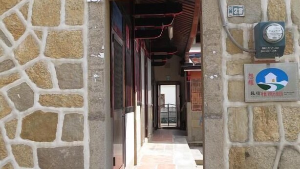 A stone-walled corridor with a tiled floor leading to a door. There are signs on the wall, including one with a blue and white logo and another with a number. - I Like B&B (Jinsha)