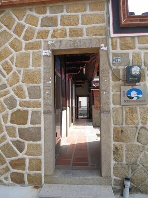 A stone-walled corridor with a tiled floor leading to a door. There are signs on the wall, including one with a blue and white logo and another with a number. - I Like B&B (Jinsha)