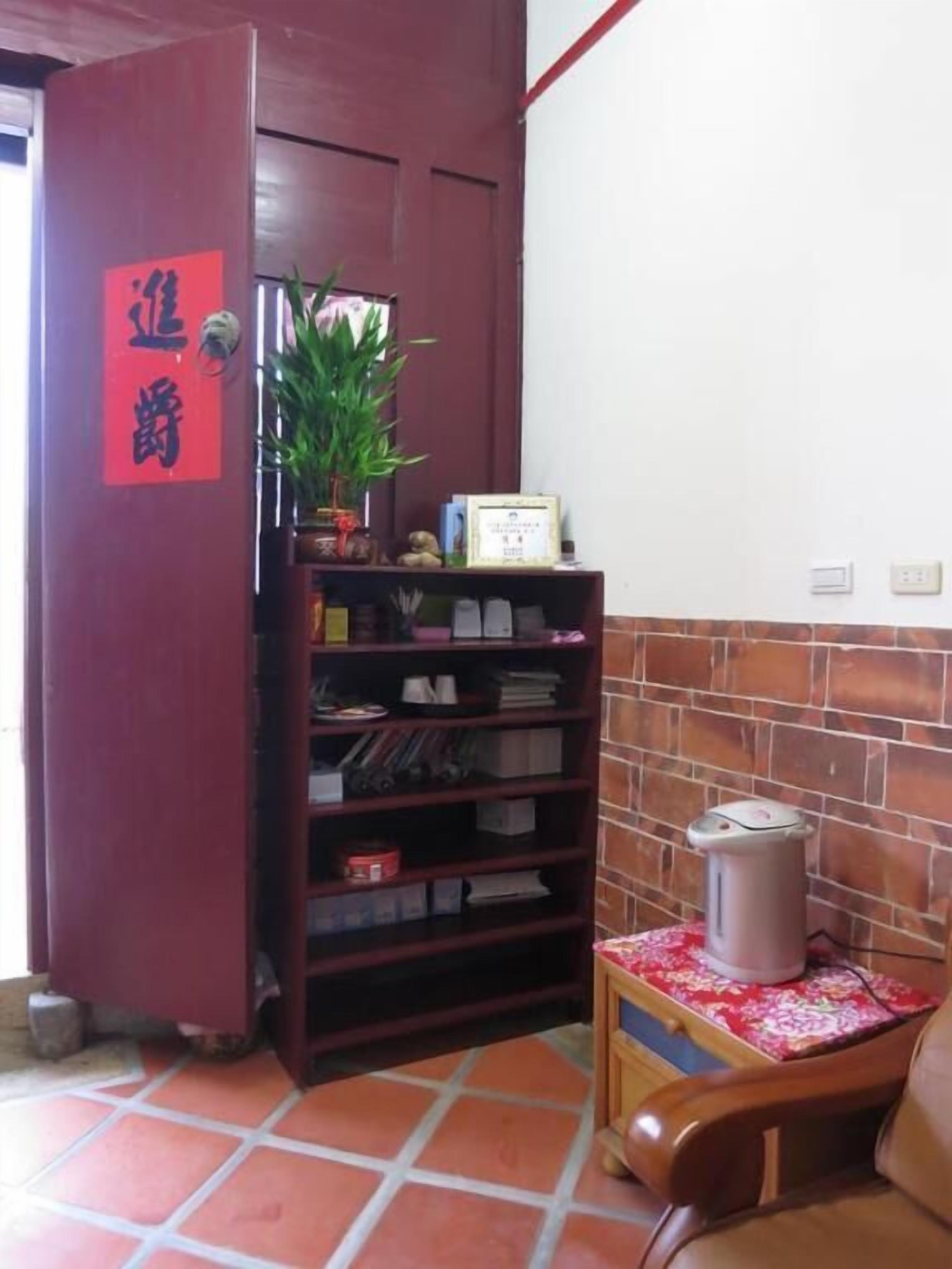 A reception area with a wooden desk, a bookshelf, a potted plant, and a red sign on the door.
