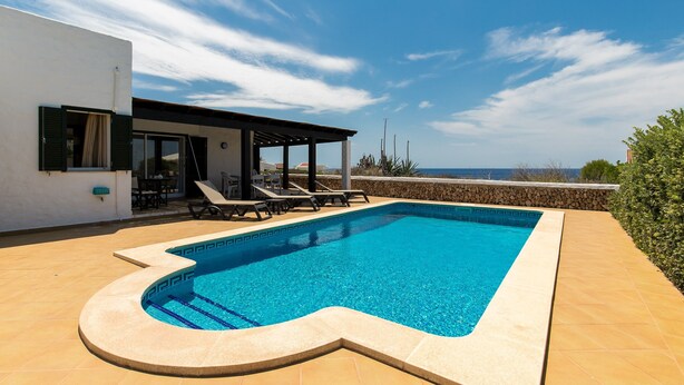 Una piscina con forma singular, una zona de estar al aire libre techada y vistas al mar.