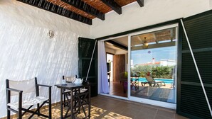 Un patio con mesa y sillas, una puerta corrediza de vidrio que da a una piscina y vistas al exterior.
