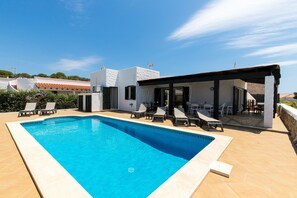 A swimming pool with lounge chairs, a covered outdoor seating area, and a view of the surrounding buildings.