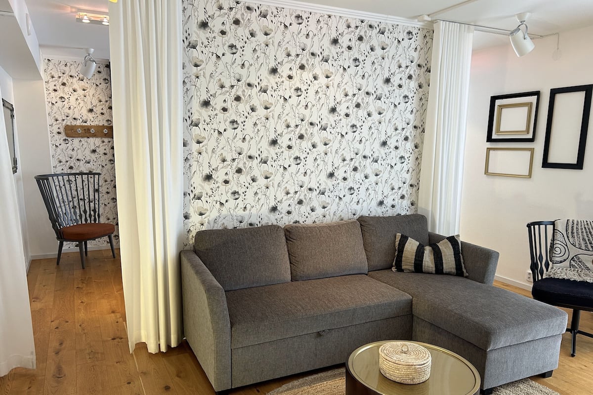 Uma sala de estar moderna com um sofá modular cinzento, uma mesa de centro redonda e um papel de parede estampado.