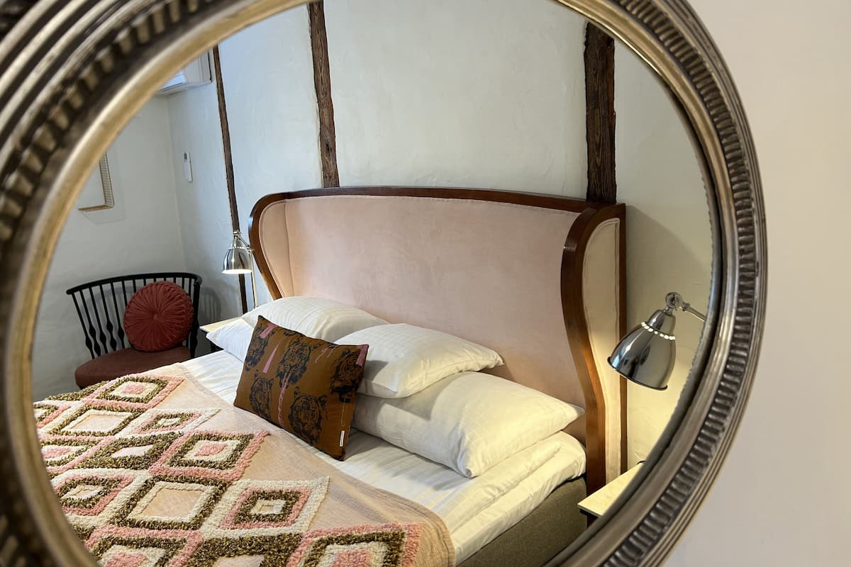 Um quarto com cama, travesseiros, abajur e espelho.
