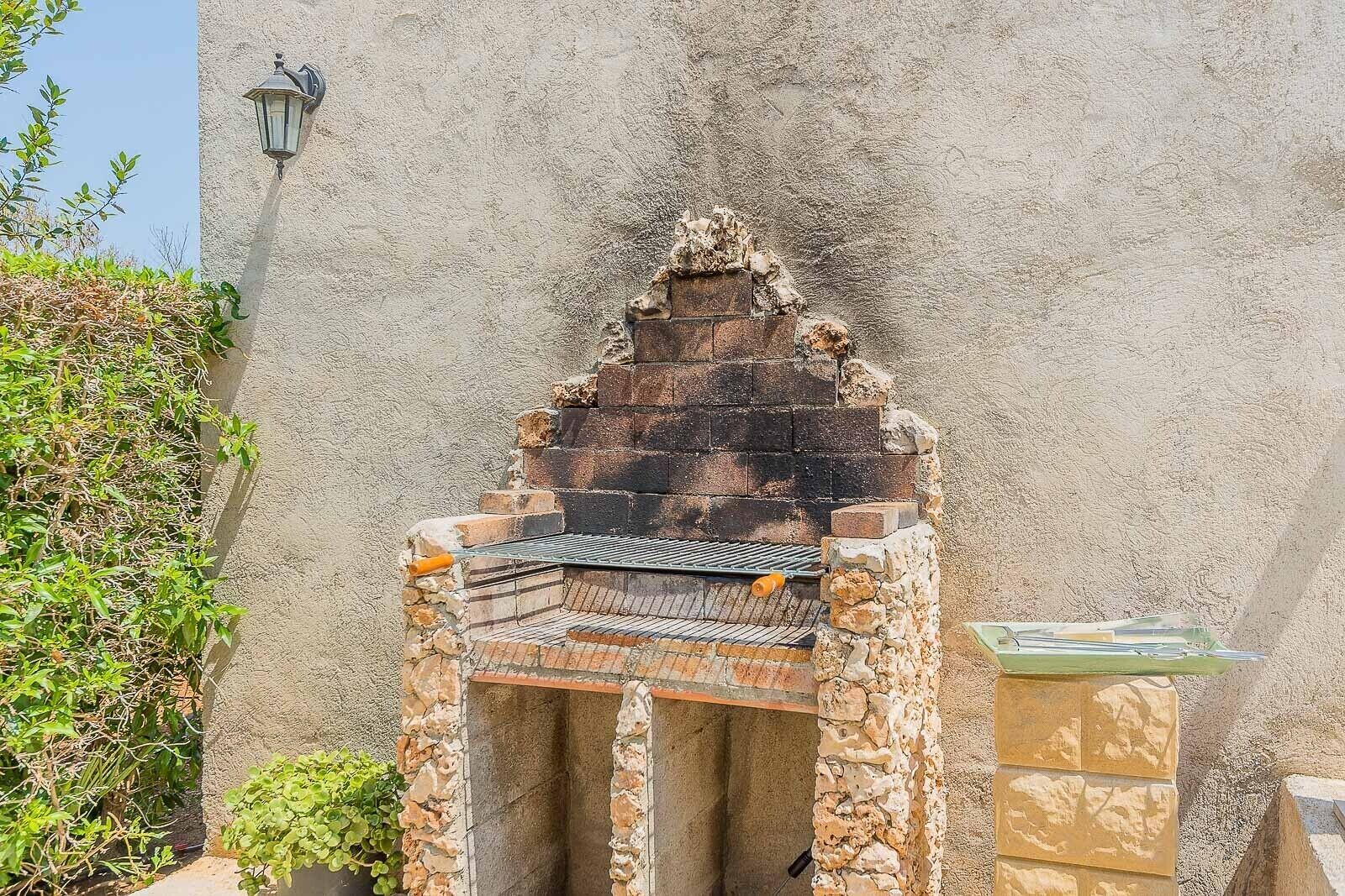 A stone-built outdoor grill with a metal grate, set against a textured wall.