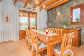 Un comedor con mesa y sillas de madera, pared de piedra y vistas al exterior.