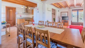 Un grand espace à manger aménagé avec du mobilier en bois, une cuisine équipée d’appareils électroménagers modernes et un salon doté d’un téléviseur.