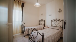 Un dormitorio con dos camas individuales, una ventana con cortinas, una lámpara colgante y adornos en la pared.