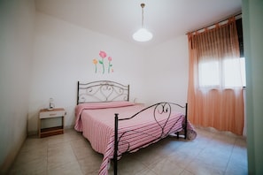 Un dormitorio con cama, mesita de noche, decoración en la pared y ventana con cortinas.