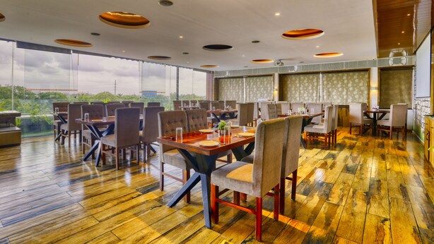 A spacious dining area with wooden flooring and multiple tables and chairs. - The Ashoka Hotel (Indore)