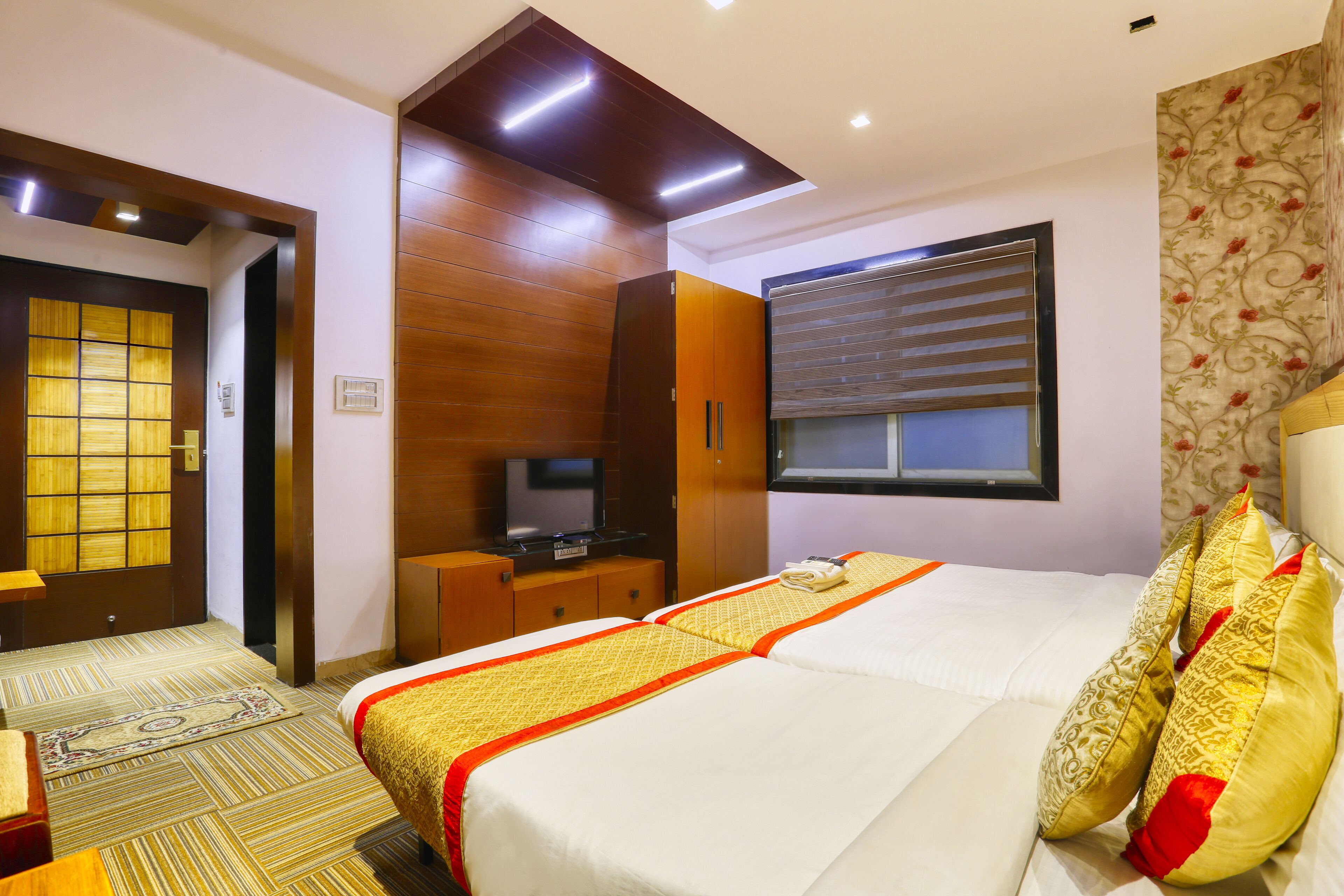 A hotel room with a bed, a television, a wardrobe, and a window with blinds.