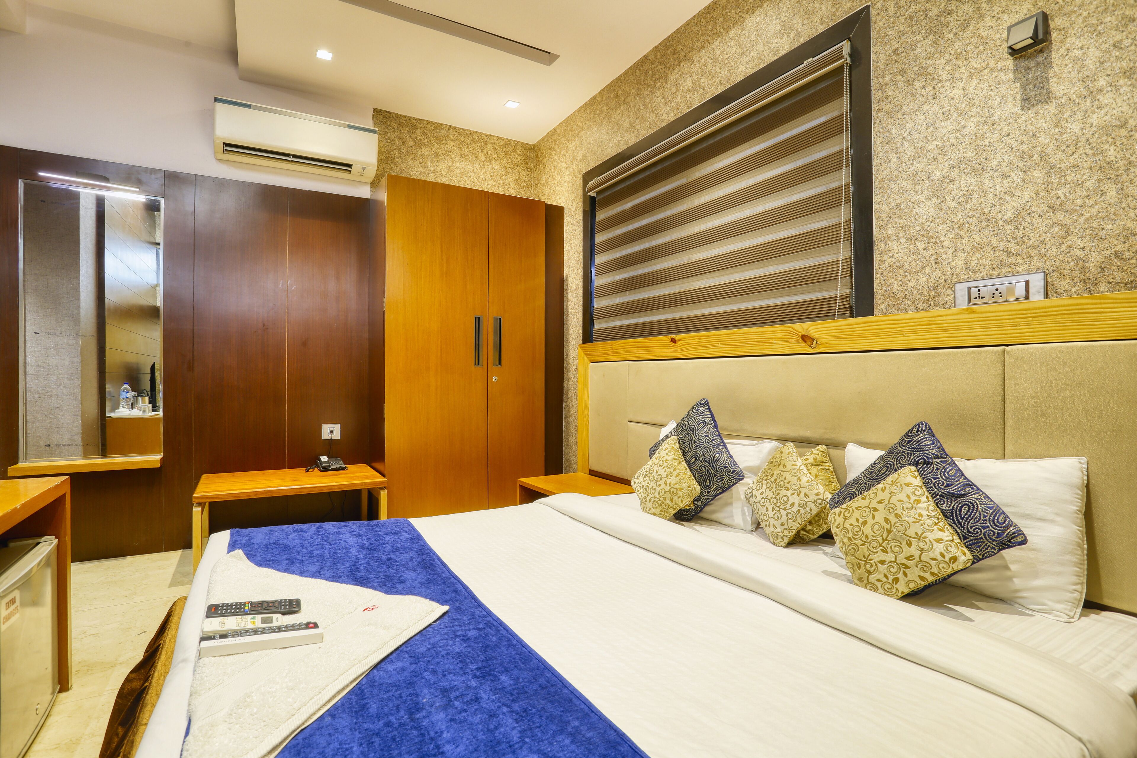 Ein Hotelzimmer mit Bett, Nachttischen, einem Kleiderschrank, einer Klimaanlage und einem Fenster mit Jalousien.