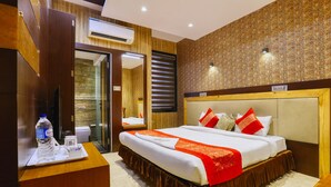 A hotel room with a large bed, a wooden headboard, a bedside table with a water bottle, and a mirror. - The Ashoka Hotel (Indore)