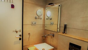 A bathroom with a white sink, two wall-mounted mirrors, a towel rack, and a shelf with toiletries. - The Ashoka Hotel (Indore)