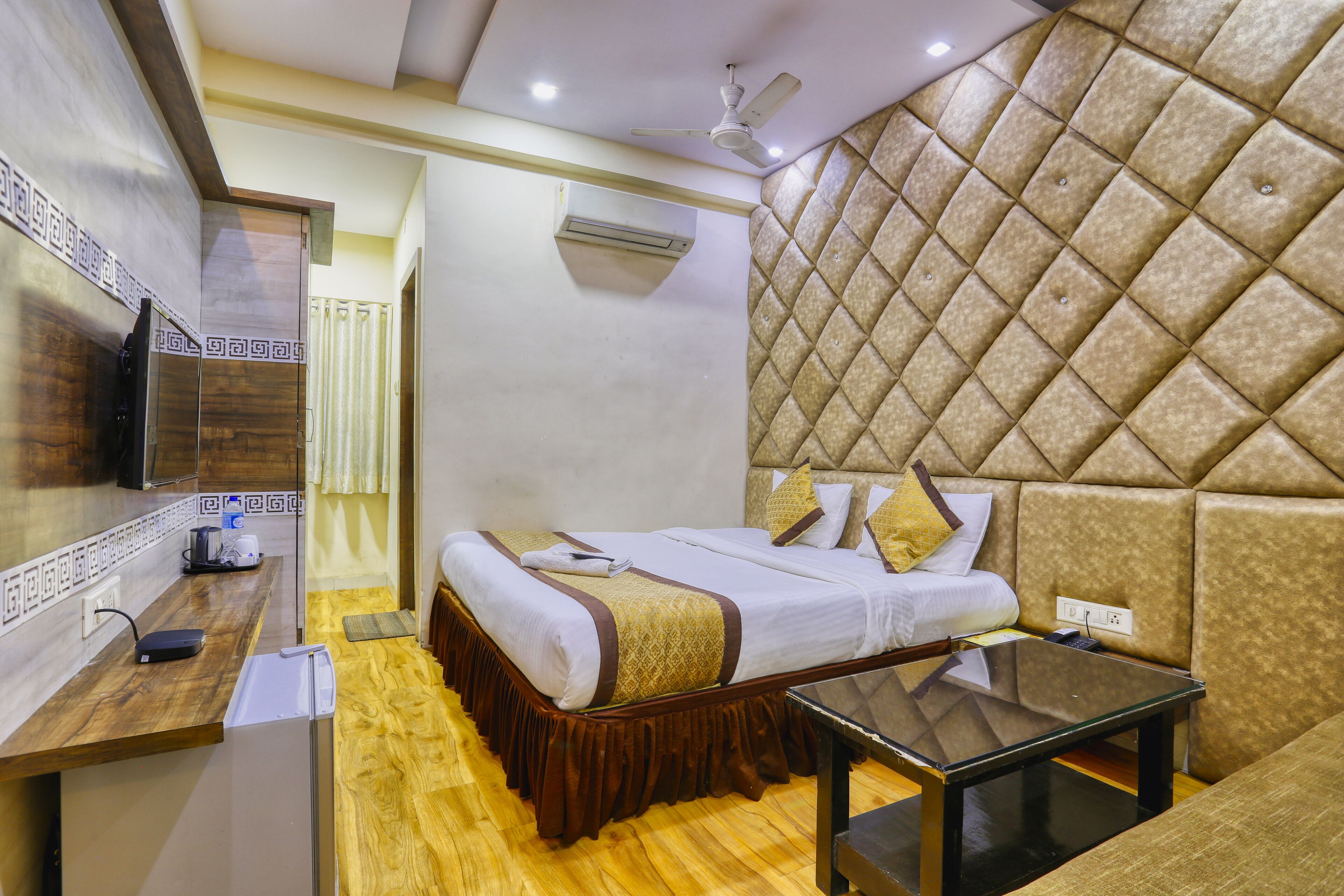 A hotel room with a bed, a desk, a television, and a wall-mounted air conditioner.