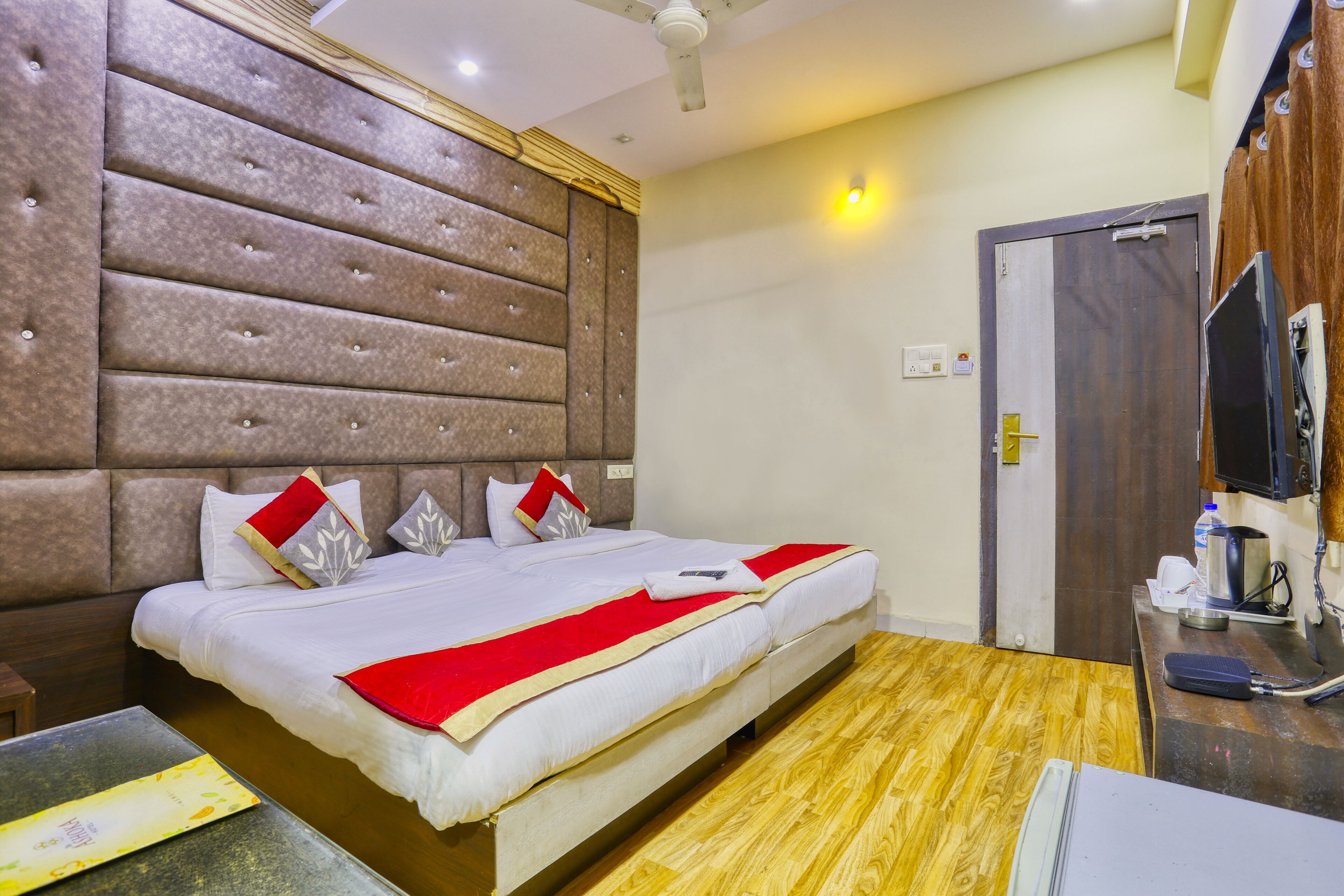 A hotel room with a large bed, a wooden floor, a television, and a desk with a chair.