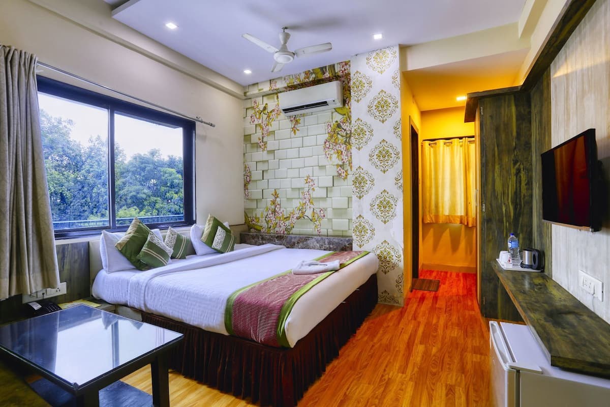 Habitación de hotel con cama, escritorio, televisor y ventana con vista a árboles.