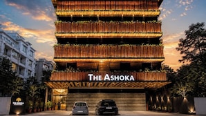 Een hotel met meerdere verdiepingen, met een modern ontwerp, een opvallende ingang en een bord met de tekst 'The Ashoka'.