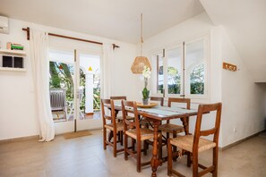 A dining area with a wooden table and chairs, a hanging light fixture, and a view through the glass doors. - Beautiful "Can Botana 7" with Wi-Fi, Pool, Air Conditioning, Balcony and Garden (Cala Sant Vicenç)