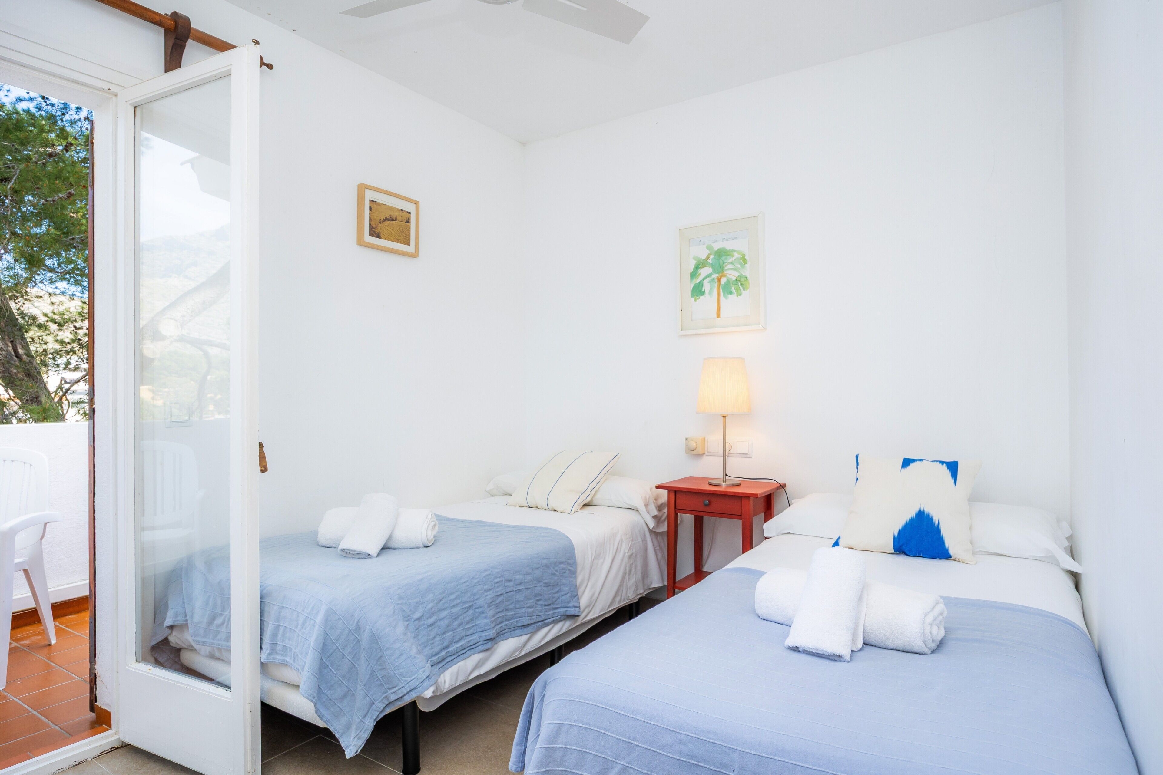 Habitación de hotel con dos camas, una mesita con una lámpara y un ventanal corredizo que da a un espacio al aire libre.