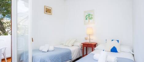 Habitación de hotel con dos camas, una mesita con una lámpara y un ventanal corredizo que da a un espacio al aire libre.