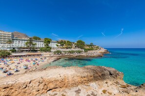Un hotel frente al mar con playa, costa rocosa y mar azul cristalino.