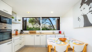 Una cocina moderna con armarios blancos, horno integrado y comedor con mesa y sillas.