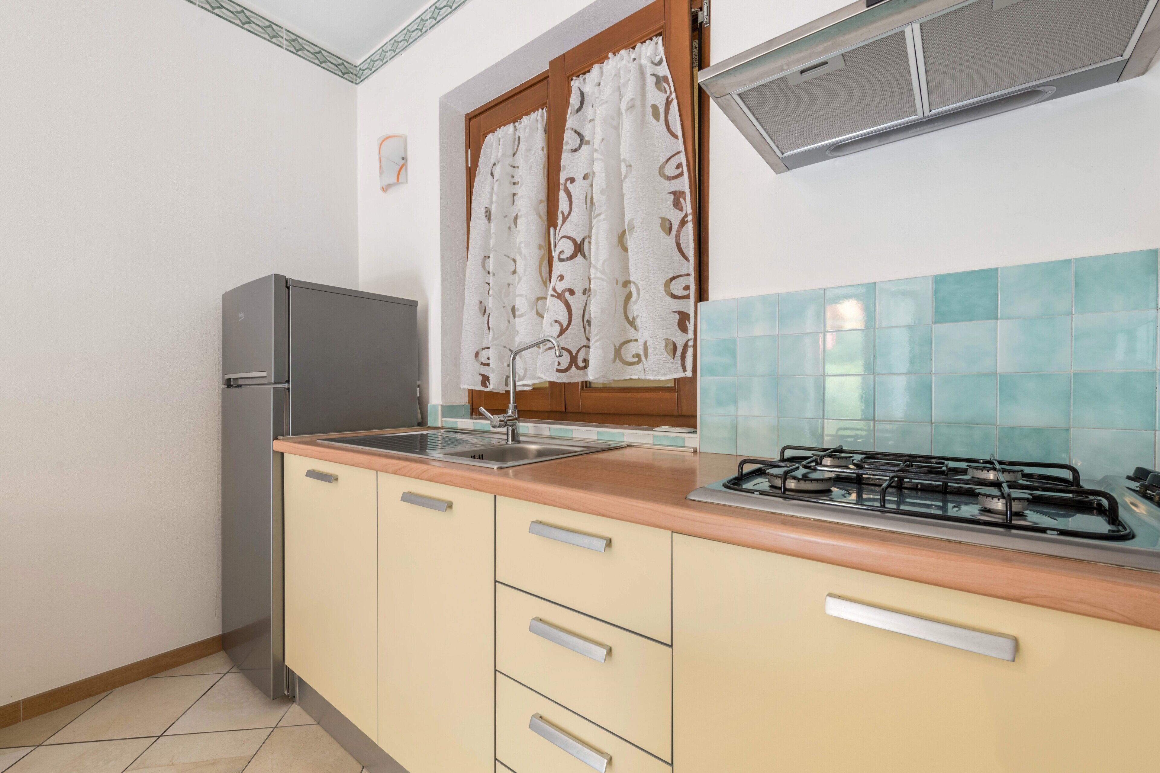 A kitchen with a refrigerator, stove, sink, and wooden cabinets.