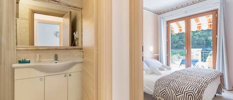 A bedroom with a bed, a bathroom with a sink and mirror, and a view of the outdoors through a sliding door.