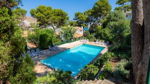 Una piscina con lettini, circondata da alberi e vista sui palazzi.