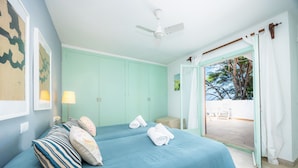 Una stanza con un letto, un ventilatore a soffitto, una porta che dà su un'area esterna e un muro decorato con quadri.