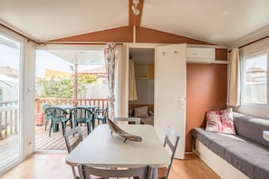 A room with a table, chairs, a sofa, a window, and an open door leading to an outdoor area with a deck and chairs.