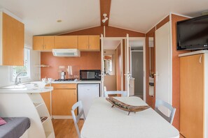 A compact kitchen with a microwave, stove, and sink, a dining area with a table and chairs, and a TV mounted on the wall.