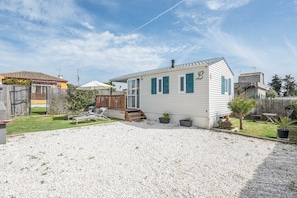 A single-story house with a gravel driveway, a wooden deck, and a small garden area with potted plants.