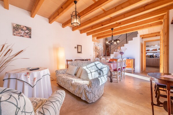 A cozy living room with a sofa, a table with a remote, and a staircase leading to a kitchen.