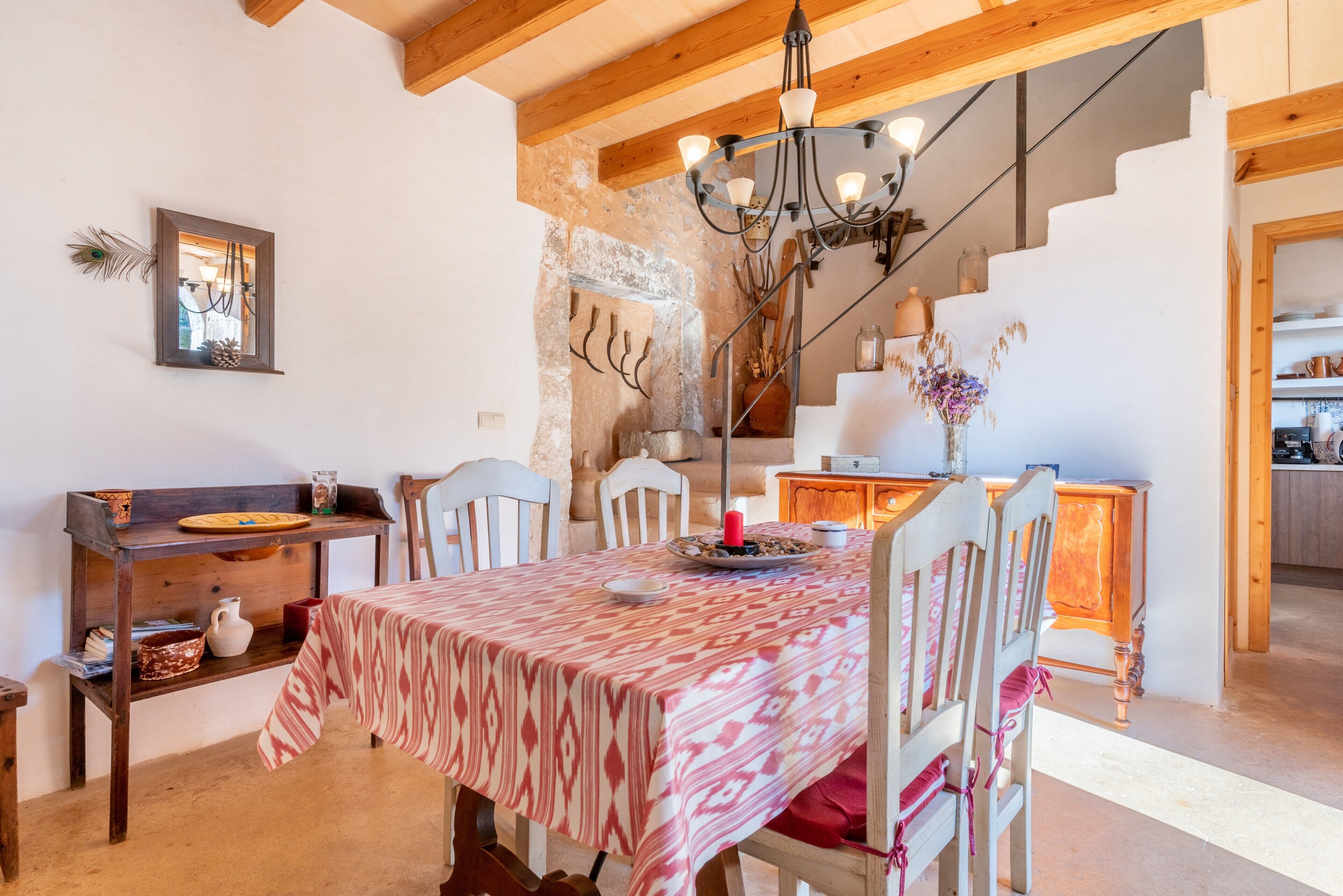 Un comedor con una mesa dispuesta para cuatro personas, sillas de madera, una araña y una pared de piedra rústica.