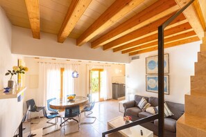 A spacious living area with a wooden ceiling, a round glass table, and a grey sofa.