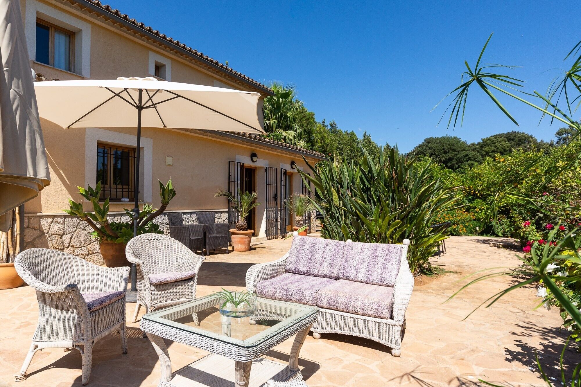 A patio with wicker furniture, a glass table, and a large umbrella.