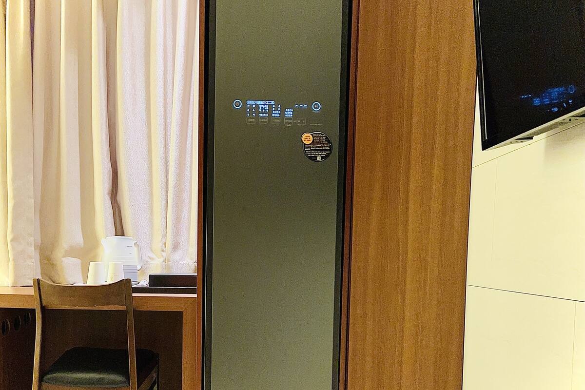 Una habitación con un escritorio de madera, una silla, una mesita con tazas y una cafetera, y un televisor montado en la pared.