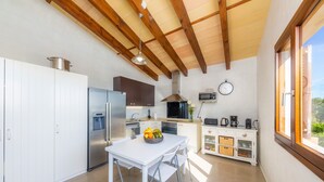 Een moderne keuken met witte kasten, een roestvrijstalen koelkast, een magnetron en een fornuis. Er staat een eettafel met stoelen en een fruitschaal.