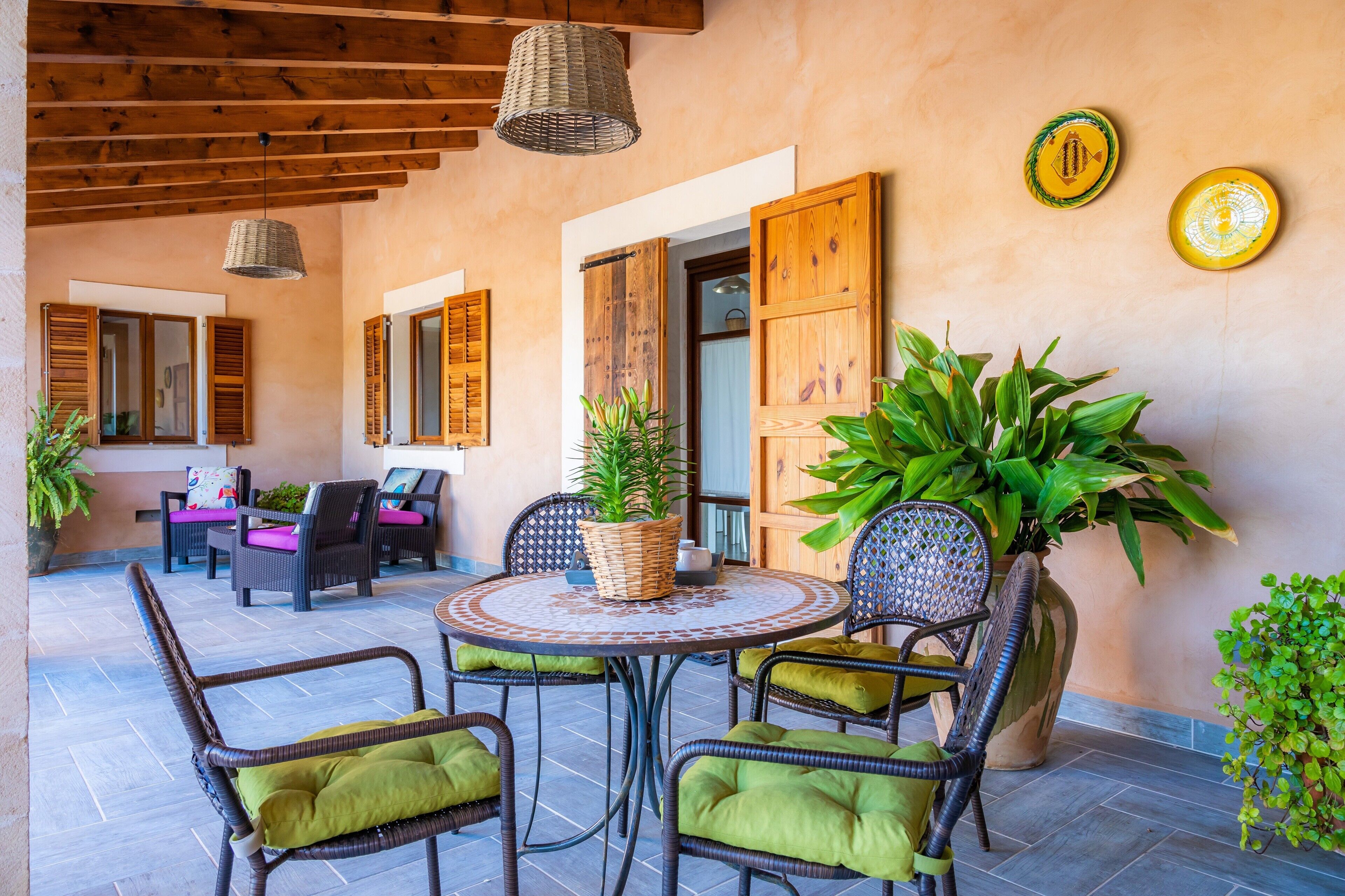 An outdoor patio area with wicker furniture, a round table, and potted plants.