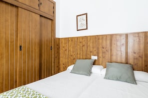 Une chambre avec une armoire en bois, un lit avec une literie blanche et un tableau encadré au mur.