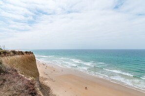 Ein Strand mit einer Klippe, dem Meer und Menschen, die entlanggehen.