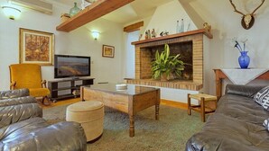 Un salon avec une cheminée, des canapés en cuir, un téléviseur et un crâne de cerf accroché au mur.