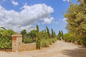 A rural road leading to a stone gate with a sign, surrounded by lush greenery and trees. - Finca Antonio for 9 persons near Buger Mallorca (Buger)