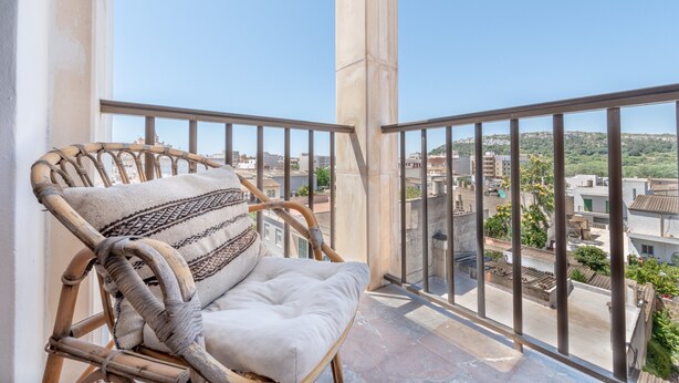 A wicker chair with a patterned cushion on a balcony with a clear view of buildings and greenery. - Modern Apartment with Balconies & Wi-Fi; Pets Allowed, Parking Available (Felanitx)